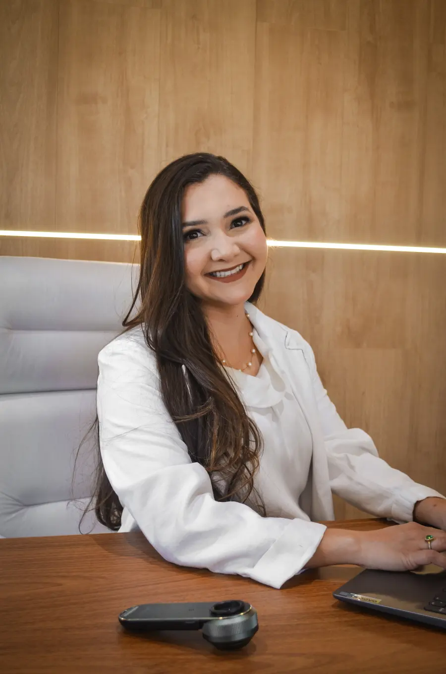 Dra. Ester Santana sentada à mesa do consultório, de jaleco branco